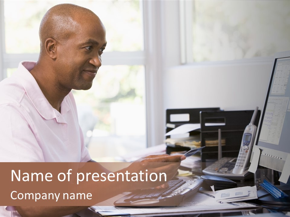 Man In Home Office Using Computer Holding Credit Card And Smiling PowerPoint Template