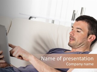 A Man Sitting On A Couch Looking At A Tablet PowerPoint Template