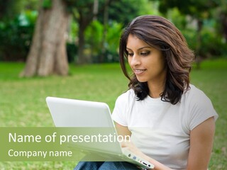 A Woman Sitting In The Grass Using A Laptop Computer PowerPoint Template