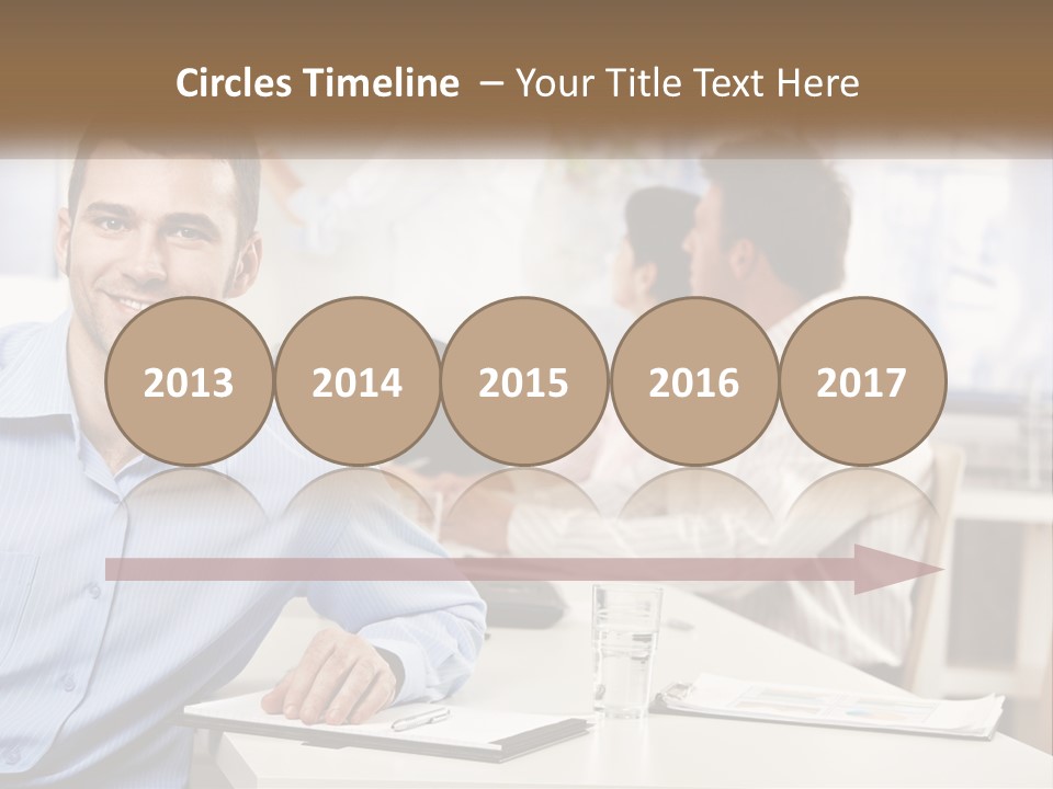 A Man Sitting At A Desk In Front Of A Group Of People PowerPoint Template