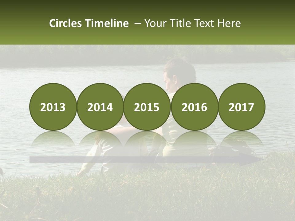 A Man And A Child Sitting On The Grass Near A Body Of Water PowerPoint Template