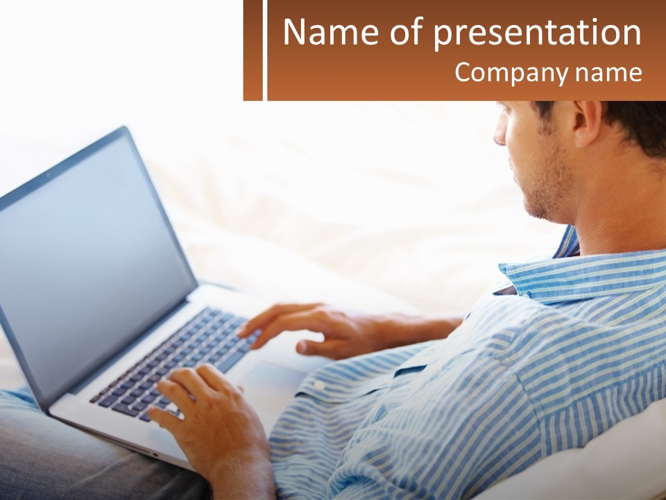 A Man Sitting On A Couch Using A Laptop Computer PowerPoint Template