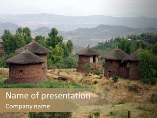 A Group Of Huts Sitting On Top Of A Lush Green Hillside PowerPoint Template