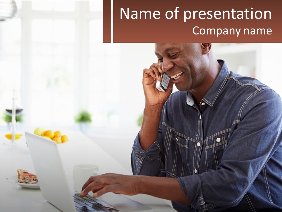A Man Talking On A Cell Phone While Using A Laptop PowerPoint Template