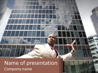 A Man In A Suit Holding Up A Red Object In Front Of A Tall Building PowerPoint Template