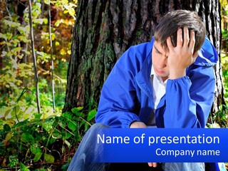 A Man In A Blue Jacket Sitting Next To A Tree PowerPoint Template