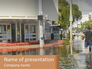 A Man Walking Down A Flooded Street Past A Building PowerPoint Template