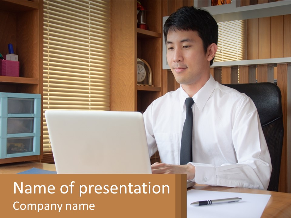 A Man Sitting At A Desk Using A Laptop Computer PowerPoint Template