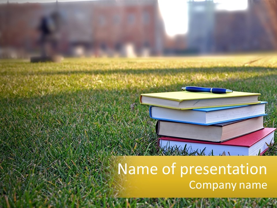 A Stack Of Books Sitting On Top Of A Lush Green Field PowerPoint Template