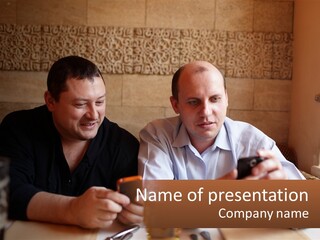Two Men Sitting At A Table Looking At A Cell Phone PowerPoint Template