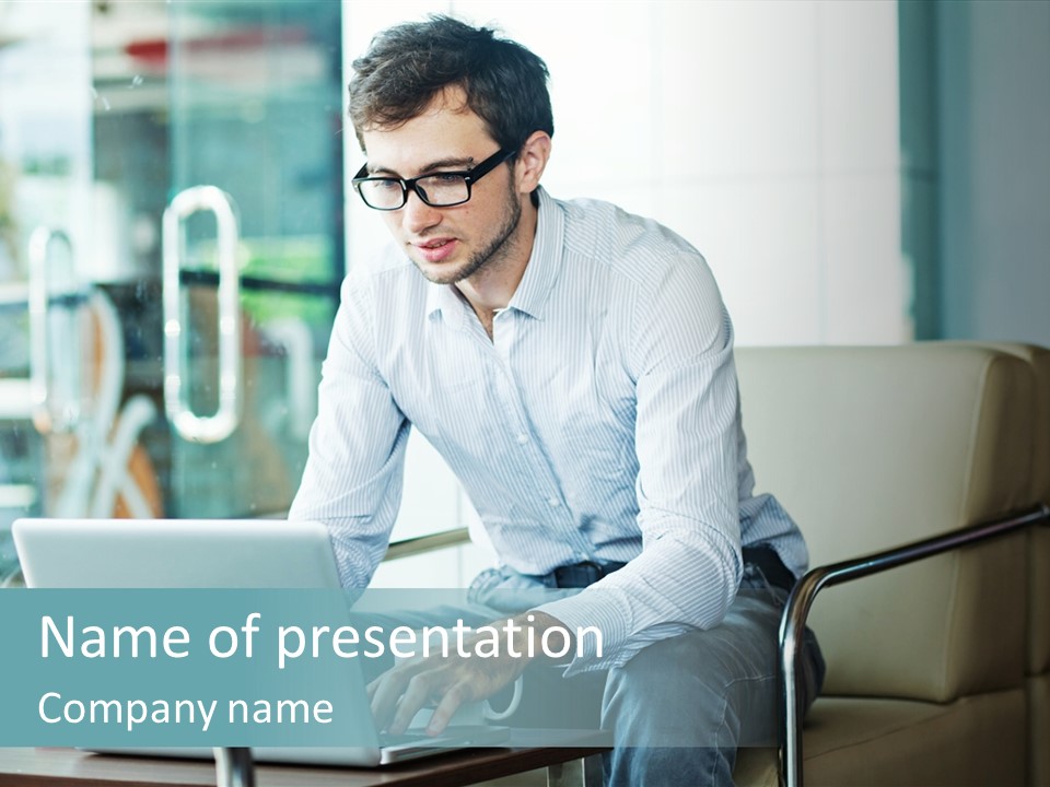A Man Sitting At A Table Using A Laptop Computer PowerPoint Template